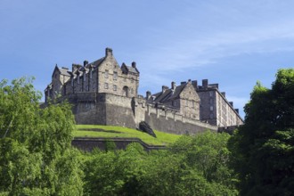 Large historic castle surrounded by greenery, under a blue sky, Edinburgh, Scotland, United Kingdom