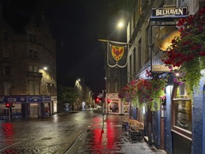 Night view of a quiet city street with wet pavement and illuminated shops. Royal Mile, Edinburgh,