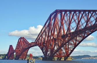 Large red metal bridge against a blue sky with white clouds, railway bridge across the Firth of