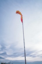 Towering flag pole with waving fabric against a blue sky