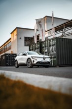 White car in front of an industrial building with containers and flags