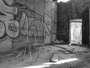 Abandoned room with graffiti and broken ceiling, empty chair ruin in the foreground, monochrome,