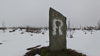 Snowy landscape with an old marker of the Rennsteig hiking trail with the letter R on it,