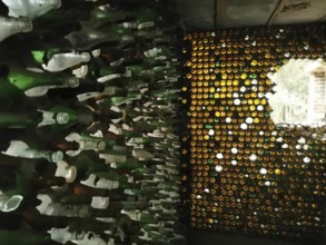 Artistic wall made of stacked glass bottles through which light shimmers, ruin house made of glass,