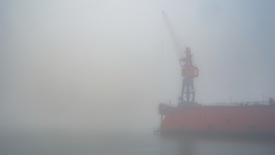 View of a dry dock at the port of America with a crane standing in fog, Cuxhaven, Lower Saxony,