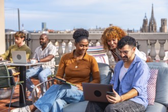 Diverse young professionals collaborating on a modern rooftop terrace, using laptops and