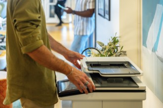 Coworker standing near a multifunction printer, opening the scanner lid to place a document for