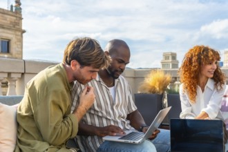 Diverse colleagues gathered on a rooftop coworking space focus on a laptop, collaborating on a