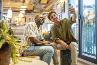Two smiling multiracial men, professional colleagues, taking a selfie together with a smartphone