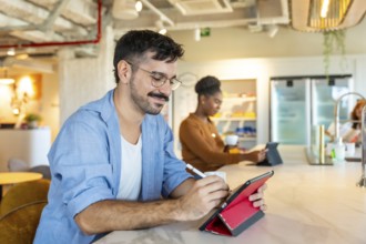 Diverse individuals making notes on a digital tablet and drinking coffee in a modern coworking