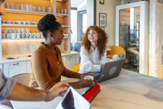 Multiracial businesswomen colleagues collaborating and discussing work around a laptop in a modern