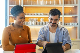 Diverse colleagues smiling and collaborating over tablets in a modern office pantry, sharing ideas