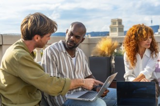 Diverse business professionals collaborating on a laptop during an informal rooftop meeting,