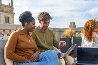Diverse colleagues collaborate on a laptop during a rooftop meeting, sharing ideas and planning in