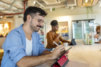 Man in casual attire smiling while using a digital tablet with a stylus to sketch ideas at a bar