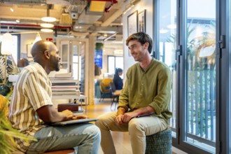 Two diverse male colleagues collaborate and chat during an informal break in a modern coworking