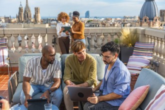 Diverse colleagues collaborate on a rooftop terrace in barcelona during a break, using laptop and