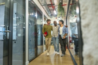 Three smiling diverse colleagues walking together embraced through a modern office building