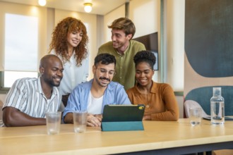 Diverse business team members gathering around a digital tablet, smiling and collaborating while