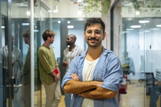 Confident male professional standing with arms crossed, smiling at the camera while his multi