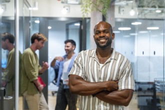 Smiling black businessman posing with arms crossed while diverse casual colleagues are