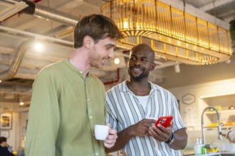 Two diverse male coworkers smiling and engaging in conversation while one holds a smartphone and