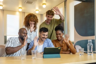 Group of diverse colleagues waving to a tablet during a business video conference in a modern