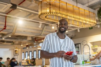 Smiling young black male professional resting in a modern coworking office space while checking his