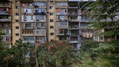 The entire façade of an old multi-storey residential building with many balconies and surrounded by