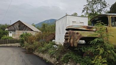 A rusty truck is parked in front of a small house on the side of the road in a village, retro