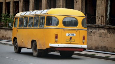 A yellow retro bus passes an old brick building along the road, Armenia