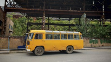 An old Nostaligian yellow bus in front of an abandoned factory, Armenia