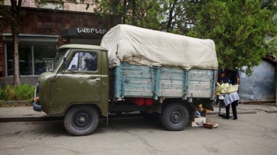 A vintage truck with a tarp on a road surrounded by trees, Armenia