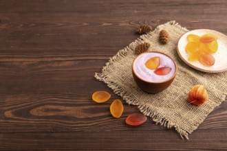 Purple Yogurt, with jelly candy on brown wooden background and linen textile, side view, copy