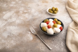 White Mozzarella cheese, with tomatoes and olives in blue bowl on brown concrete background and