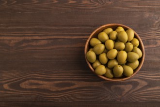 Fresh green olives in wooden bowl on brown wooden background. Top view, flat lay, copy space
