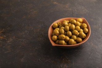 Fresh green olives in ceramic clay bowl on black concrete background. side view, copy space