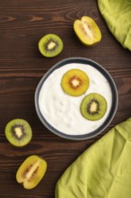 Yogurt, with kiwi in blue bowl on brown wooden background and green linen textile, top view, flat