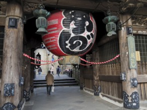 A large temple with an impressive lantern and traditional wooden construction, people enter the