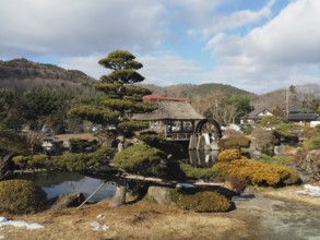 Japanese garden with traditional house and well-kept trees against mountain backdrop, Oshino