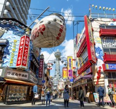 Lots of colorful signs in a pedestrian zone with shops and restaurants, behind Tsutenkaku Tower,