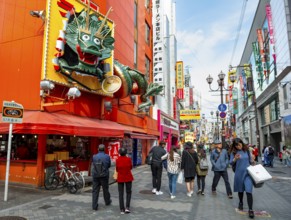 Dragon figure at a restaurant, lots of colorful signs in a pedestrian zone with shops and