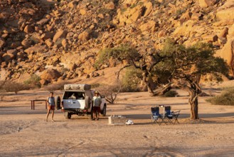 Camping in the Spitzkoppe desert under a tree next to a vehicle, surrounded by impressive rock