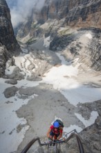 Mountaineers climb a ladder on the Via Ferrata Oliva Detassis via ferrata, rocky mountain peaks and