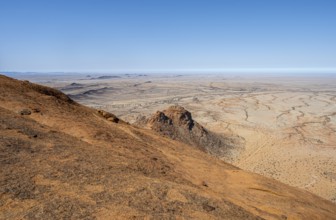 View from a hill over the endless dry desert landscape under blue sky, Spitzkoppe, Namibia