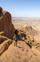 Young woman hiking on rocky hill under blue sky in dry landscape, Spitzkoppe, Namibia