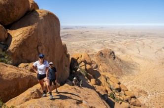 Tourists hiking on a rock with a view of a vast desert landscape, Spitzkoppe, Namibia
