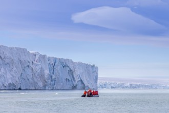 Eco-tourists in Zodiac boat and Brasvellbreen glacier wall from ice cap Austfonna debouching into