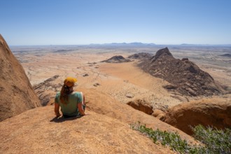 Woman sitting on rocks and enjoying the view over the barren desert landscape of Spitzkoppe,
