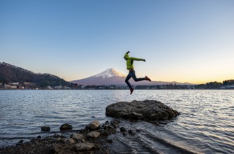 Young man jumping on rocks in Lake Kawaguchi, view of Mount Fuji volcano at sunset, Yamanashi